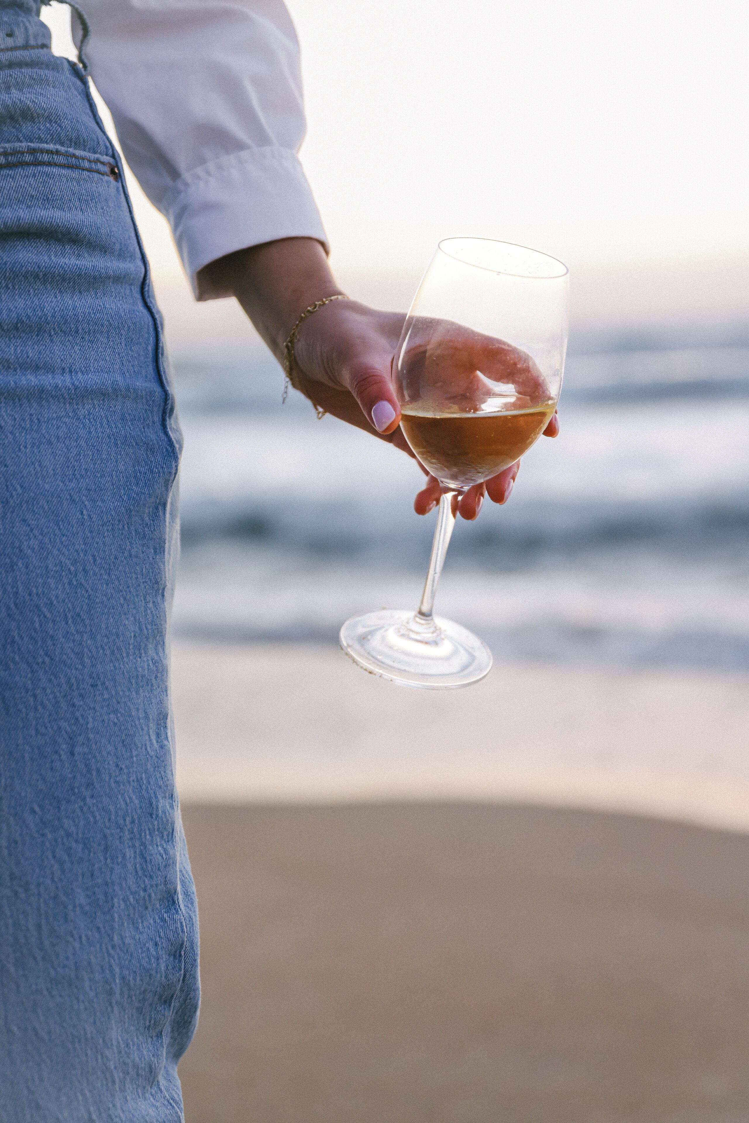A person holding a wine glass with a beach and ocean in the background.