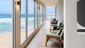 A corridor with large windows overlooking the ocean, wooden flooring, and green upholstered chairs. - Monterey Beach Hotel, A Tribute Portfolio Hotel (Monterey)
