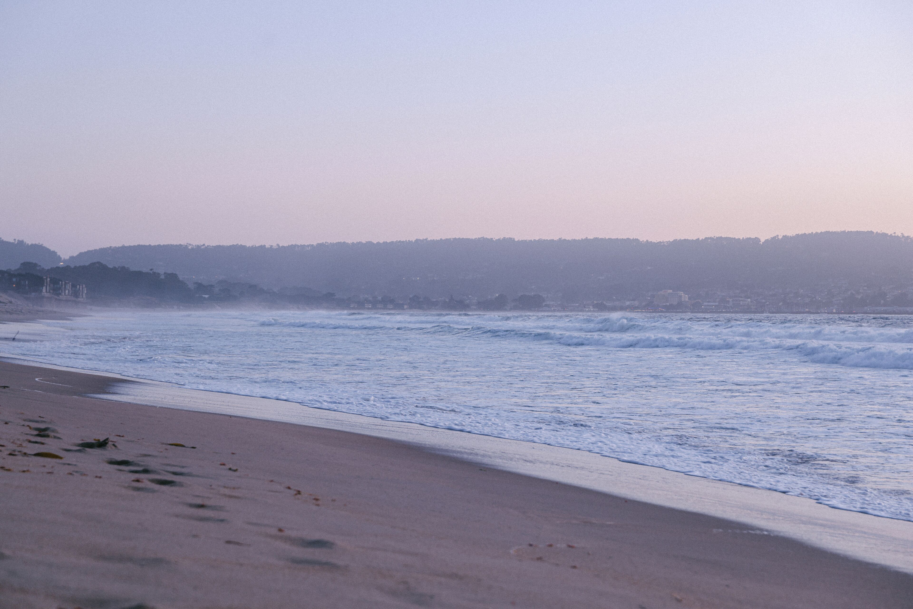 Une plage avec des vagues, une rive sablonneuse et une colline qui se dessine à l’horizon.