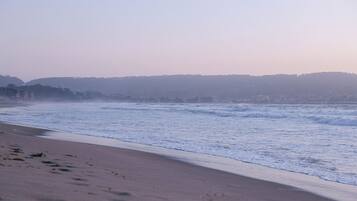 Une plage avec des vagues, une rive sablonneuse et une colline qui se dessine à l’horizon.