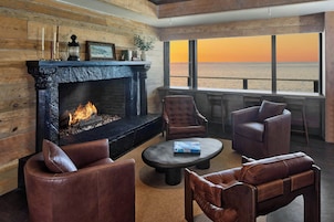 Un salón acogedor con chimenea, sofás de cuero y vista al océano al atardecer.
