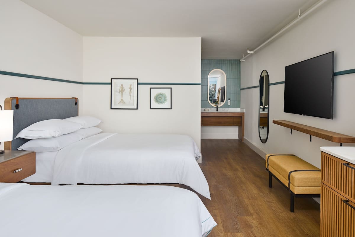 A hotel room with two beds, a wooden bench, a TV, and a mirror.