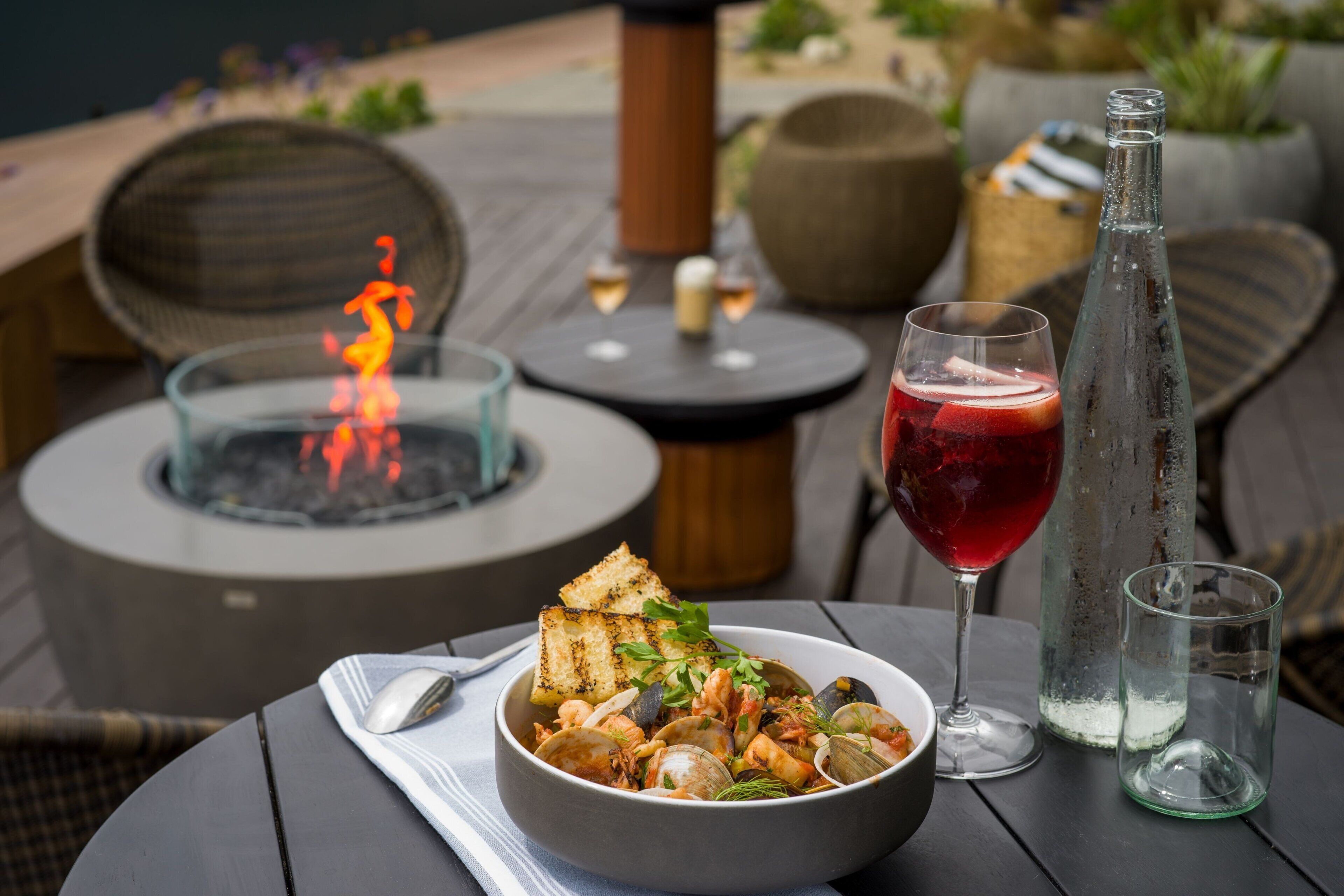 A dining table with a bowl of seafood, a glass of red drink, and a bottle of water.