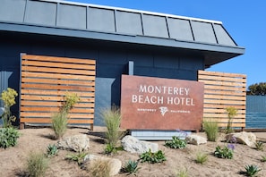 The exterior of Monterey Beach Hotel with a signboard, wooden fence, and desert landscaping.