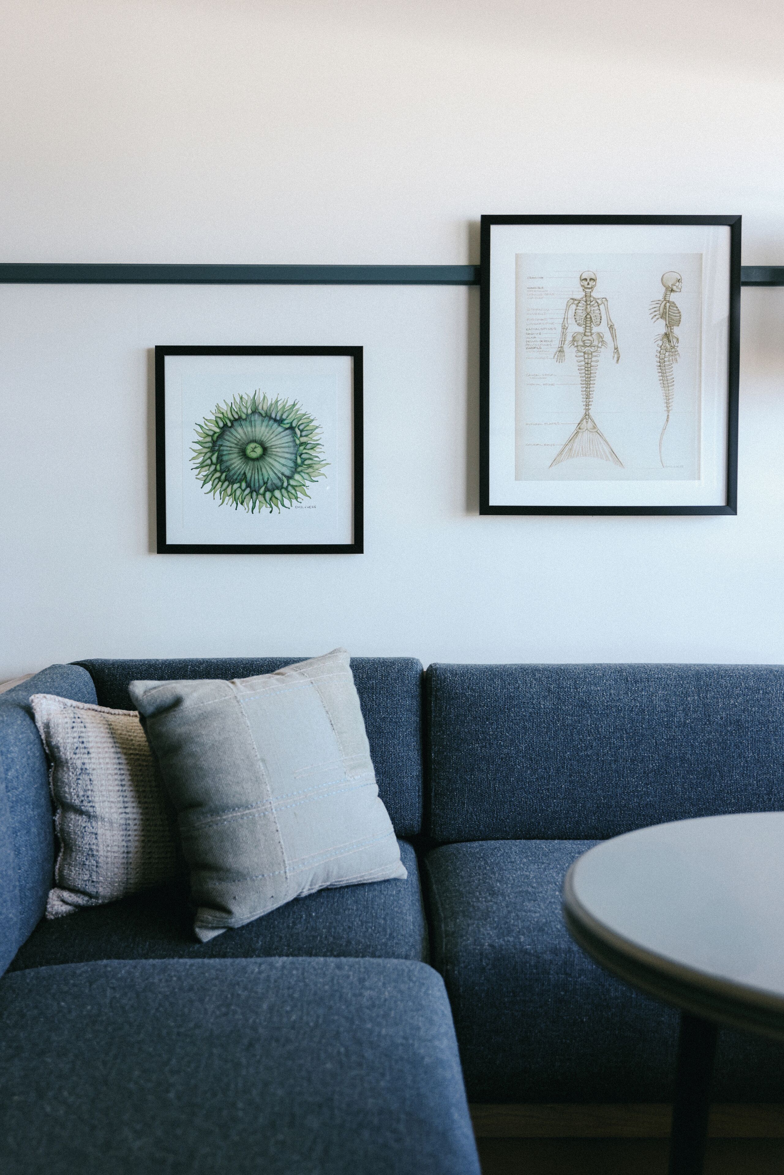 A room with a blue sofa, a round table, and two framed artworks on the wall.