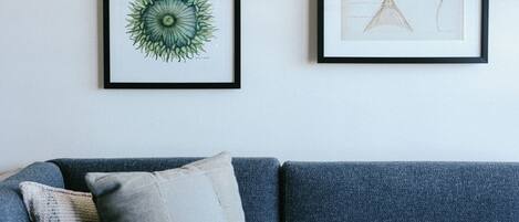 A room with a blue sofa, a round table, and two framed artworks on the wall.