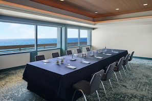 A conference room with a long table, chairs, and large windows overlooking the ocean.