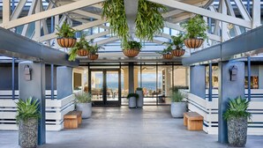 A spacious lobby with a high ceiling, large windows, and hanging planters. - Monterey Beach Hotel, A Tribute Portfolio Hotel (Monterey)