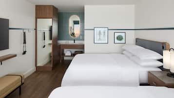 A hotel room with a bed, bedside table, lamp, and a mirror. There is a bench and a shelf with toiletries.