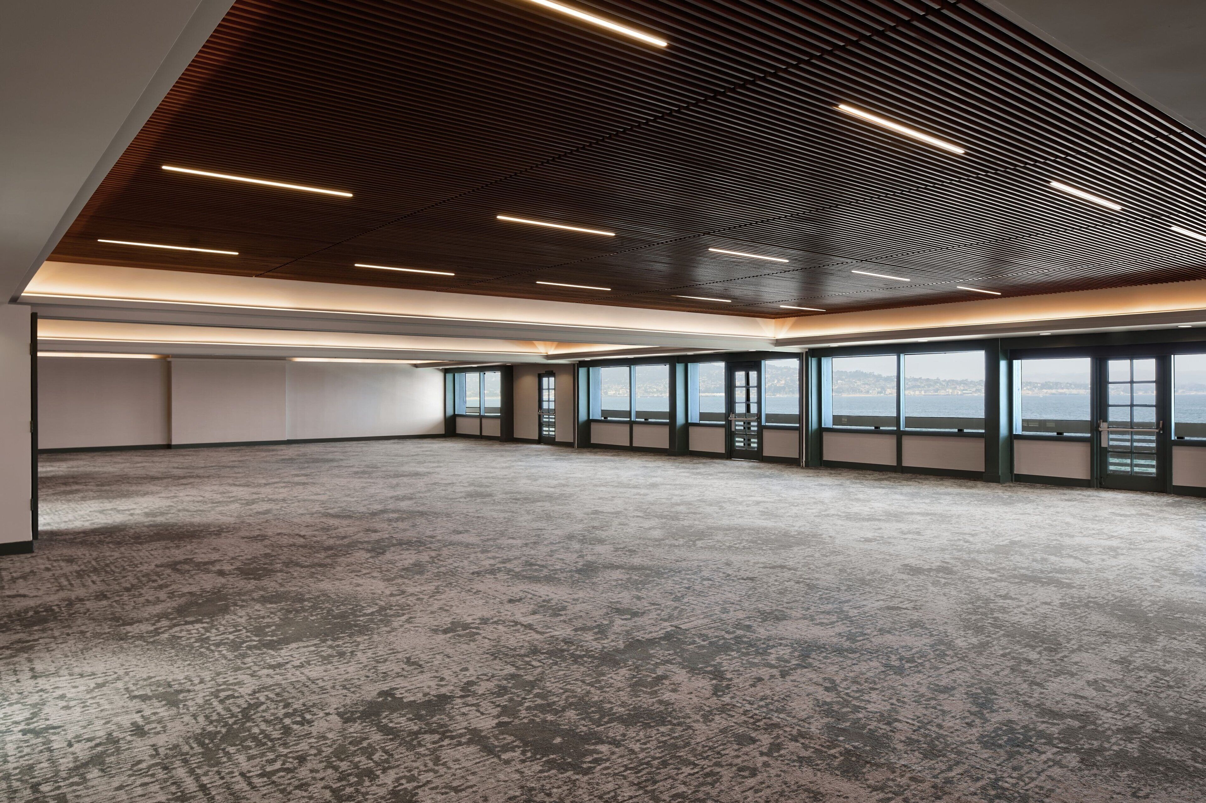A spacious, modern office with a high ceiling, large windows, and a concrete floor.