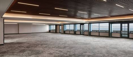 A spacious, modern office with a high ceiling, large windows, and a concrete floor.