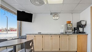 Un restaurante con mostrador, sillas, televisor montado en la pared, reloj y máquina de café.