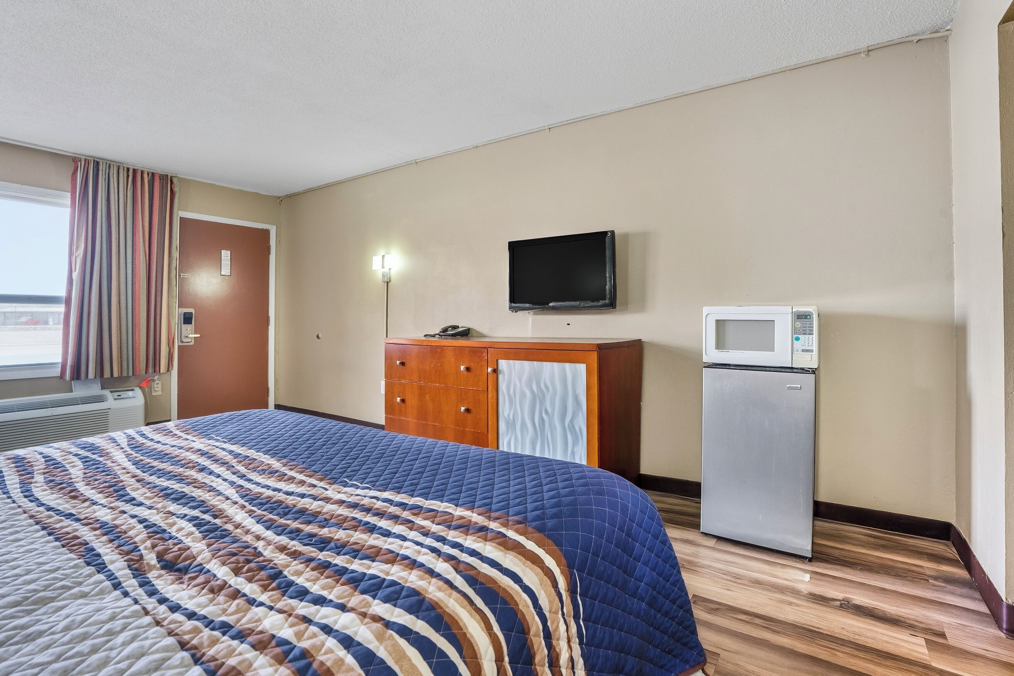 A hotel room with a bed, a wooden cabinet, a television, and a refrigerator.
