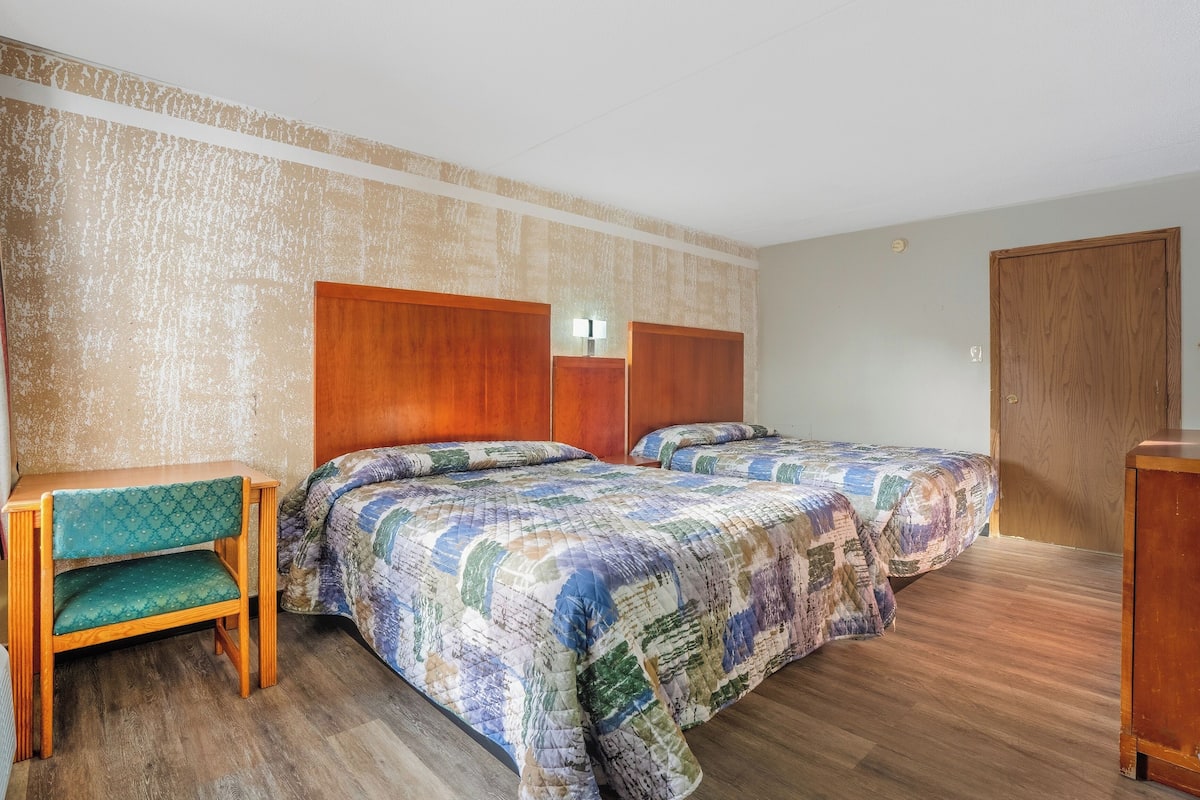 A room with two beds, a wooden desk, and a chair.