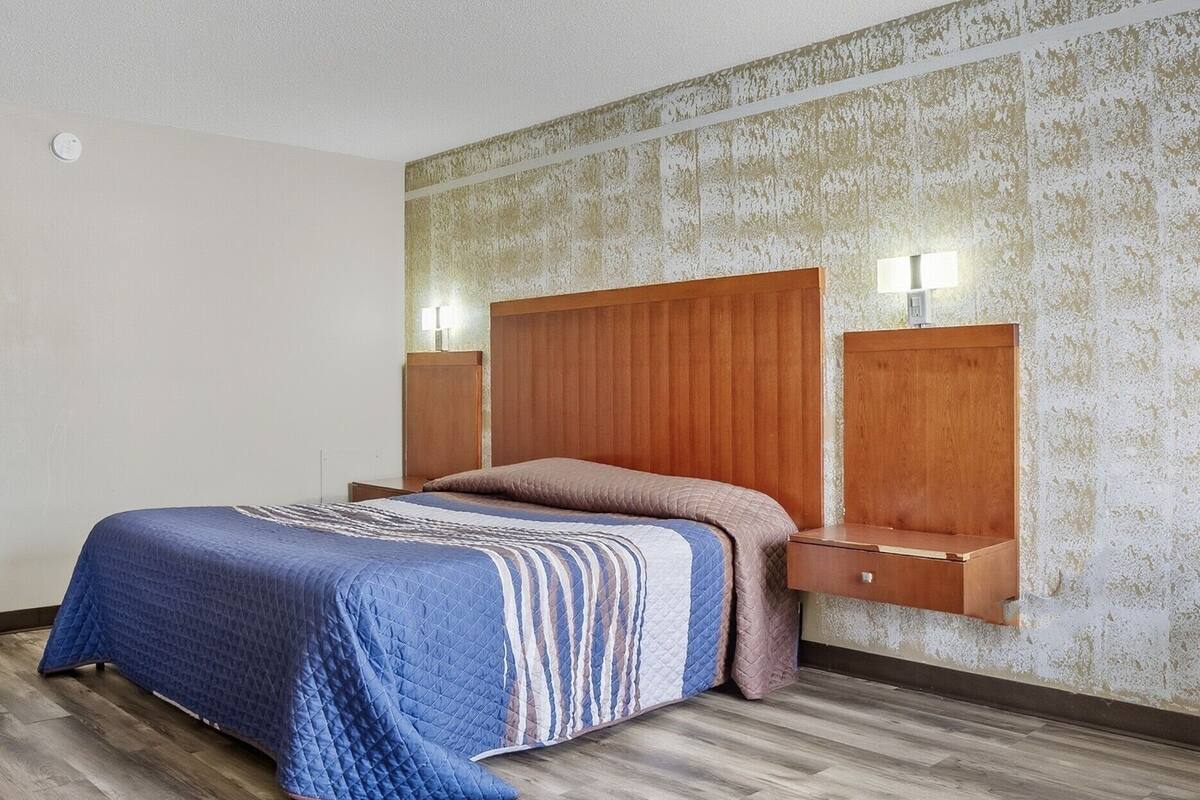 A hotel room with a wooden headboard, a quilted bedspread, and two bedside tables with lamps.