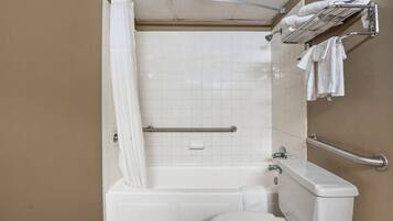 A bathroom with a bathtub, toilet, and handrails.