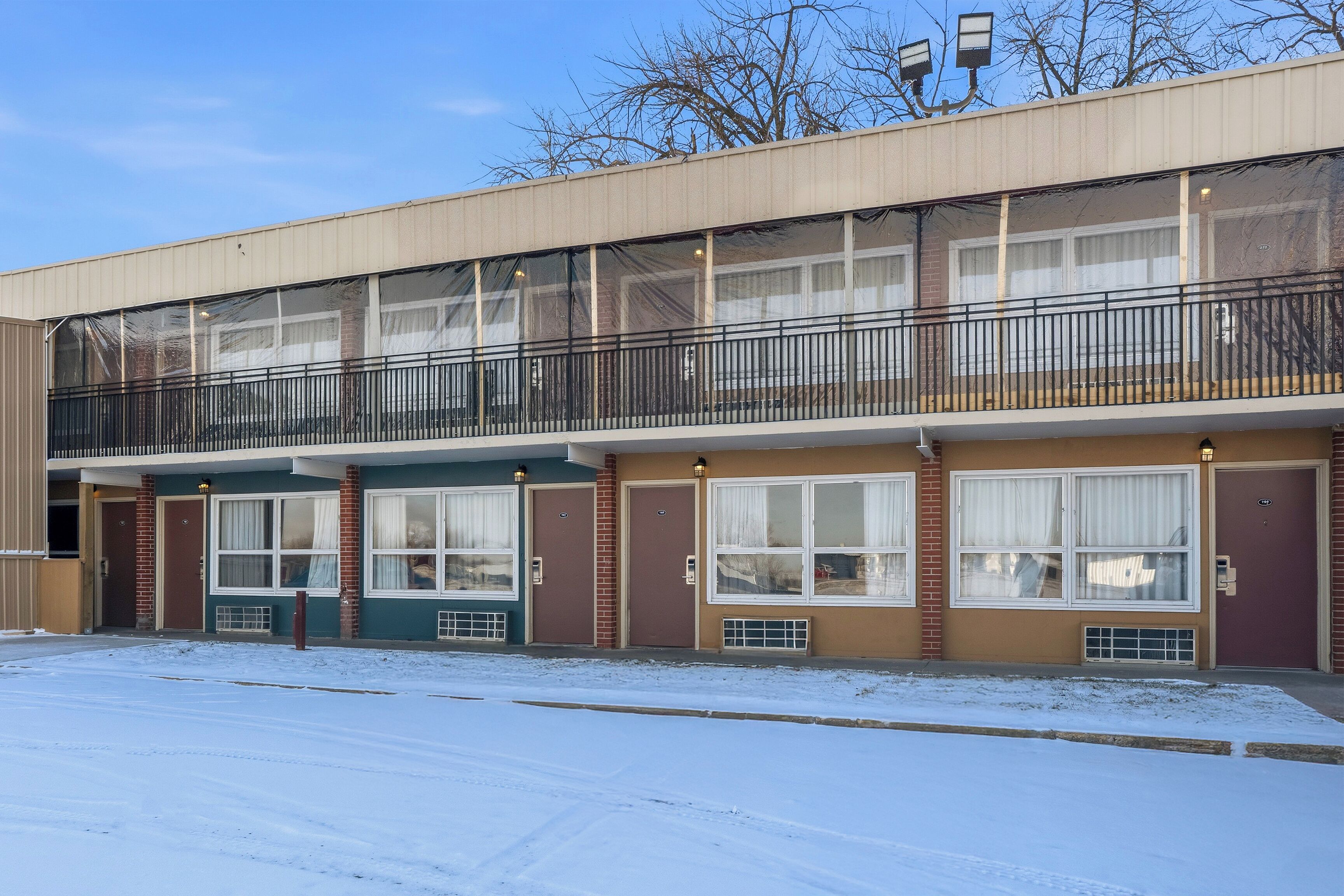 A multi-story building with a balcony, large windows, and a snow-covered ground.