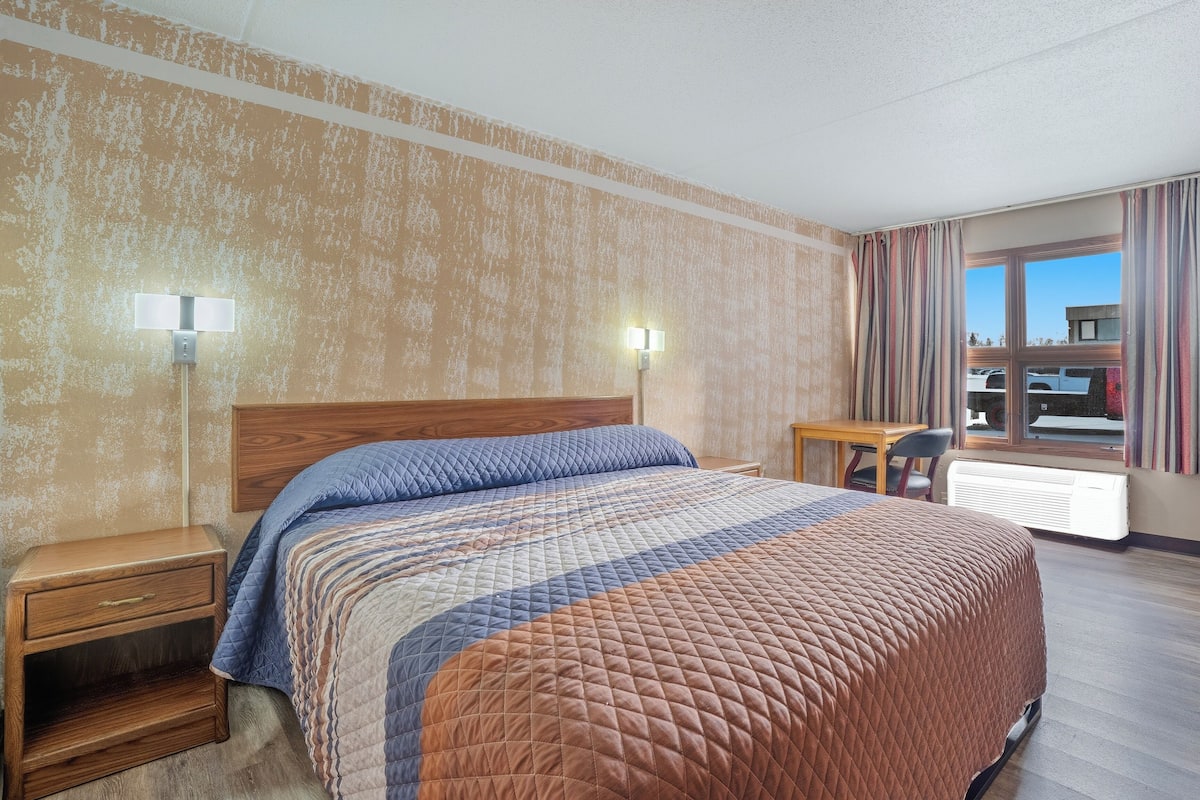 A hotel room with a large bed, two bedside tables, a desk, and a chair.