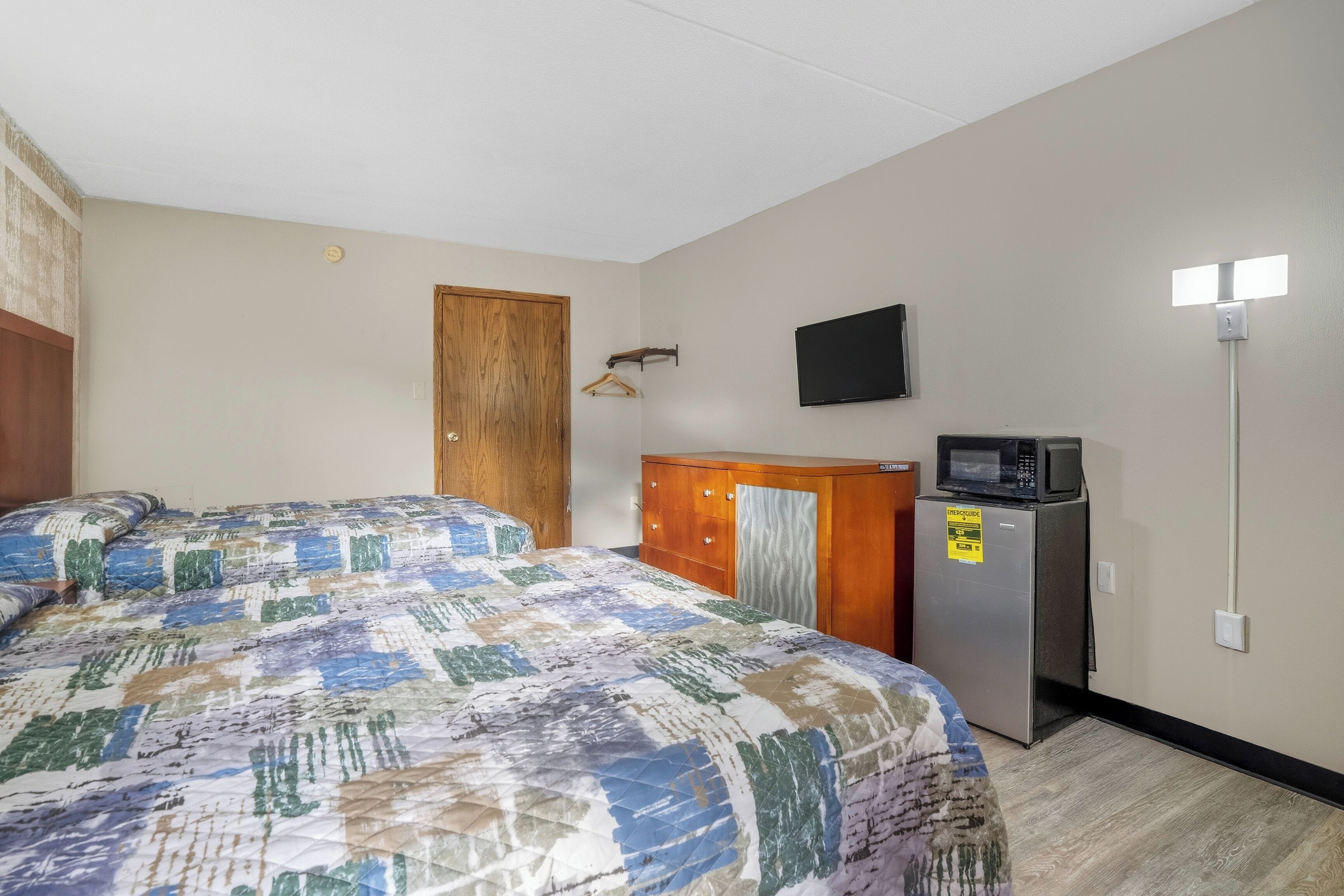 A hotel room with a bed, a wooden wardrobe, a microwave, and a television on the wall.