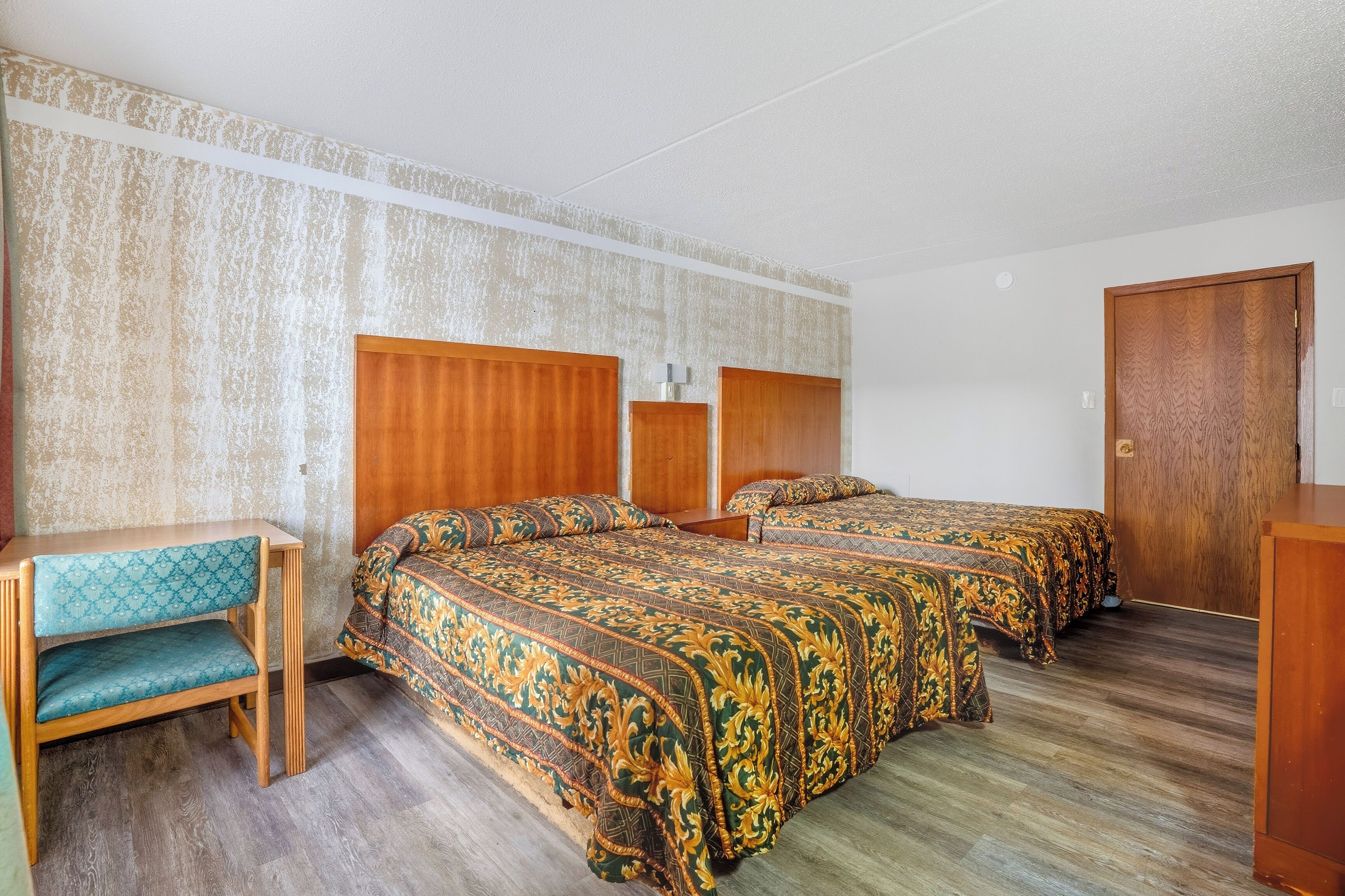 Habitació d'hotel amb llit de fusta, un petit escriptori i un armari.