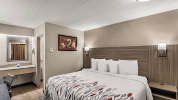 Habitación de hotel con cama, escritorio, silla, espejo y lámpara de pared.