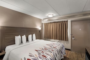 A hotel room with a large bed, a bedside table, a nightstand, a lamp, a window with curtains, and a door.