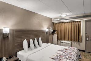 A hotel room with a large bed, a bedside table with a phone, a wall-mounted air conditioner, and a window with curtains. - Red Roof Inn Enfield (Enfield)