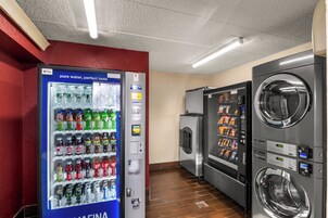 Máquina expendedora con diversas bebidas e instalaciones de lavandería con secadoras y lavadoras.