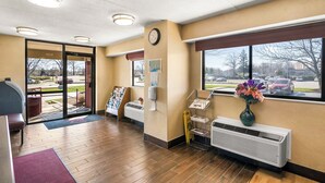 A reception area with a wooden floor, a clock, a window with a view of the parking lot, and a wall-mounted air conditioning unit. - Red Roof Inn Enfield (Enfield)