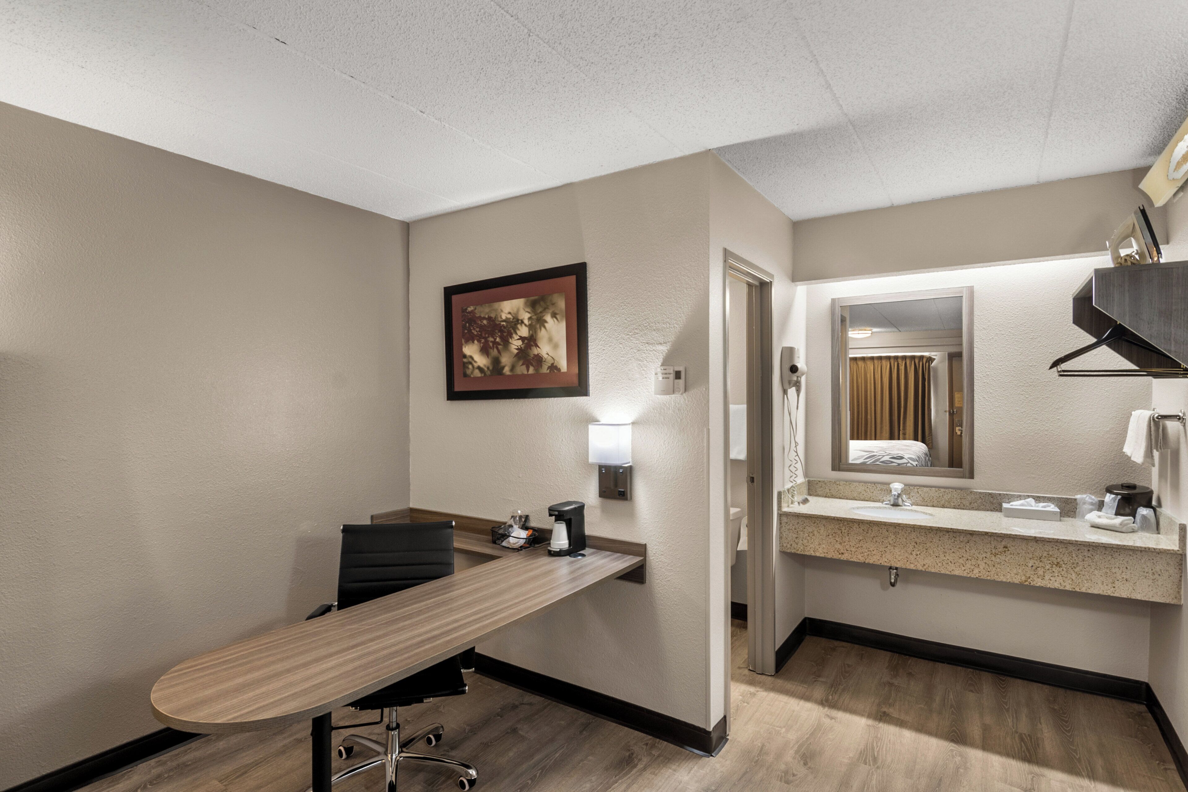 A hotel room with a desk, chair, and a large mirror.