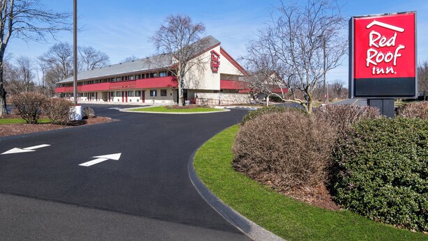 A Red Roof Inn with a red and white facade, a parking lot with directional arrows, and a clear blue sky. - Red Roof Inn Enfield (Enfield)