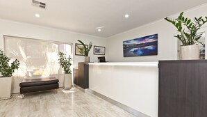 A reception area with a marble floor, a bench, a reception desk, framed pictures, and potted plants. - Morphettville Motor Inn (Camden Park)