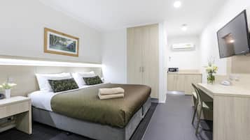 Una habitación de hotel moderna con cama, mesita de noche, escritorio, silla y televisor.