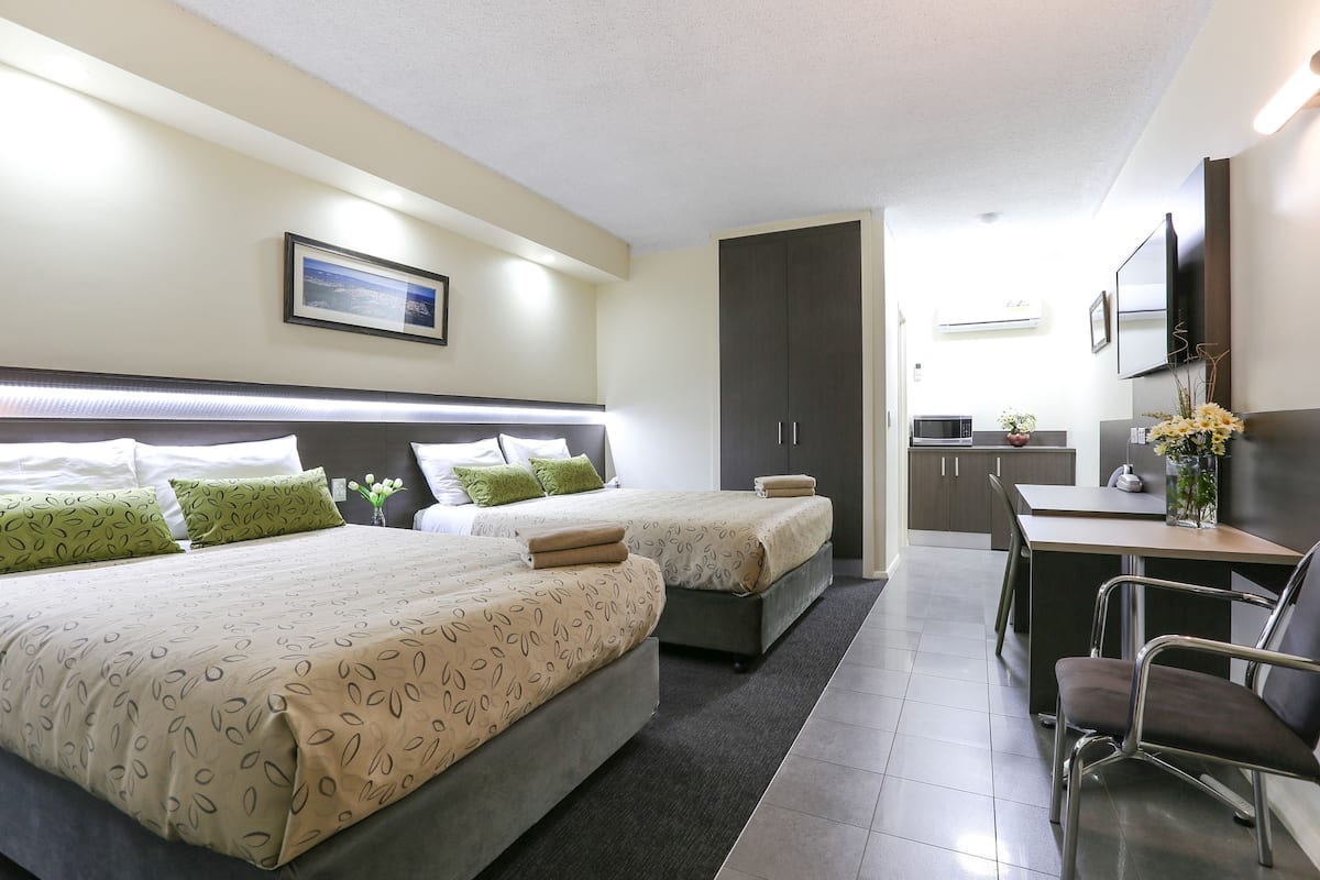 A hotel room with two beds, a desk, a chair, a TV, and a framed picture on the wall.