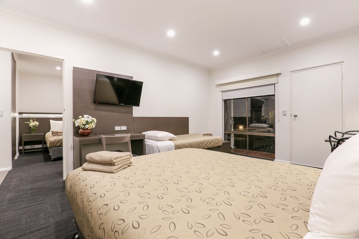 A hotel room with a large bed, a TV mounted on the wall, a desk with a chair, and a window with a view of the city.
