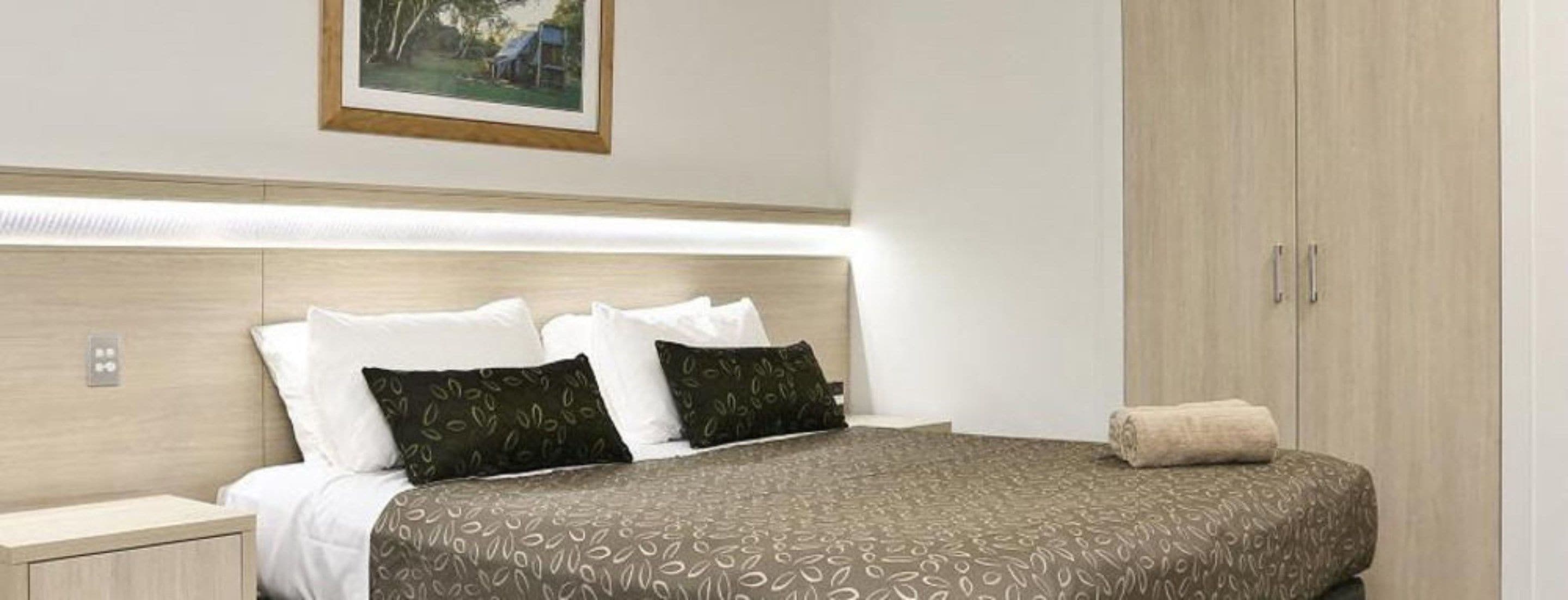 A neatly made bed with patterned bedding, a bedside table, and a wardrobe.