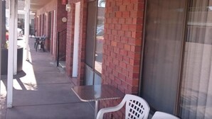A covered outdoor area with brick walls, a glass door, and a table with chairs. - Morphettville Motor Inn (Camden Park)
