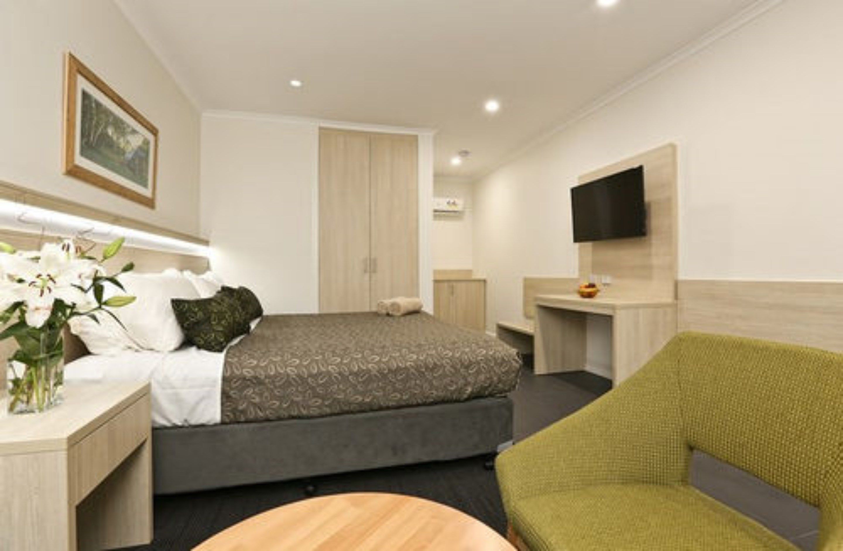 A modern hotel room with a bed, a desk, a chair, and a TV mounted on the wall.