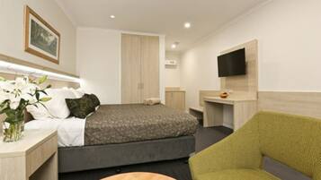 A modern hotel room with a bed, a desk, a chair, and a TV mounted on the wall.