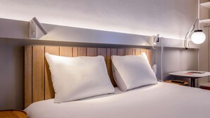 A hotel room with a wooden headboard, two pillows, a bedside table, and a lamp. - ibis La Rochelle Centre Historique Hotel (La Rochelle)