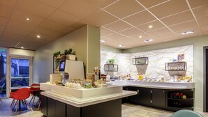 A modern cafe with a central island counter, seating area, and a decorative wall with shelves. - ibis La Rochelle Centre Historique Hotel (La Rochelle)