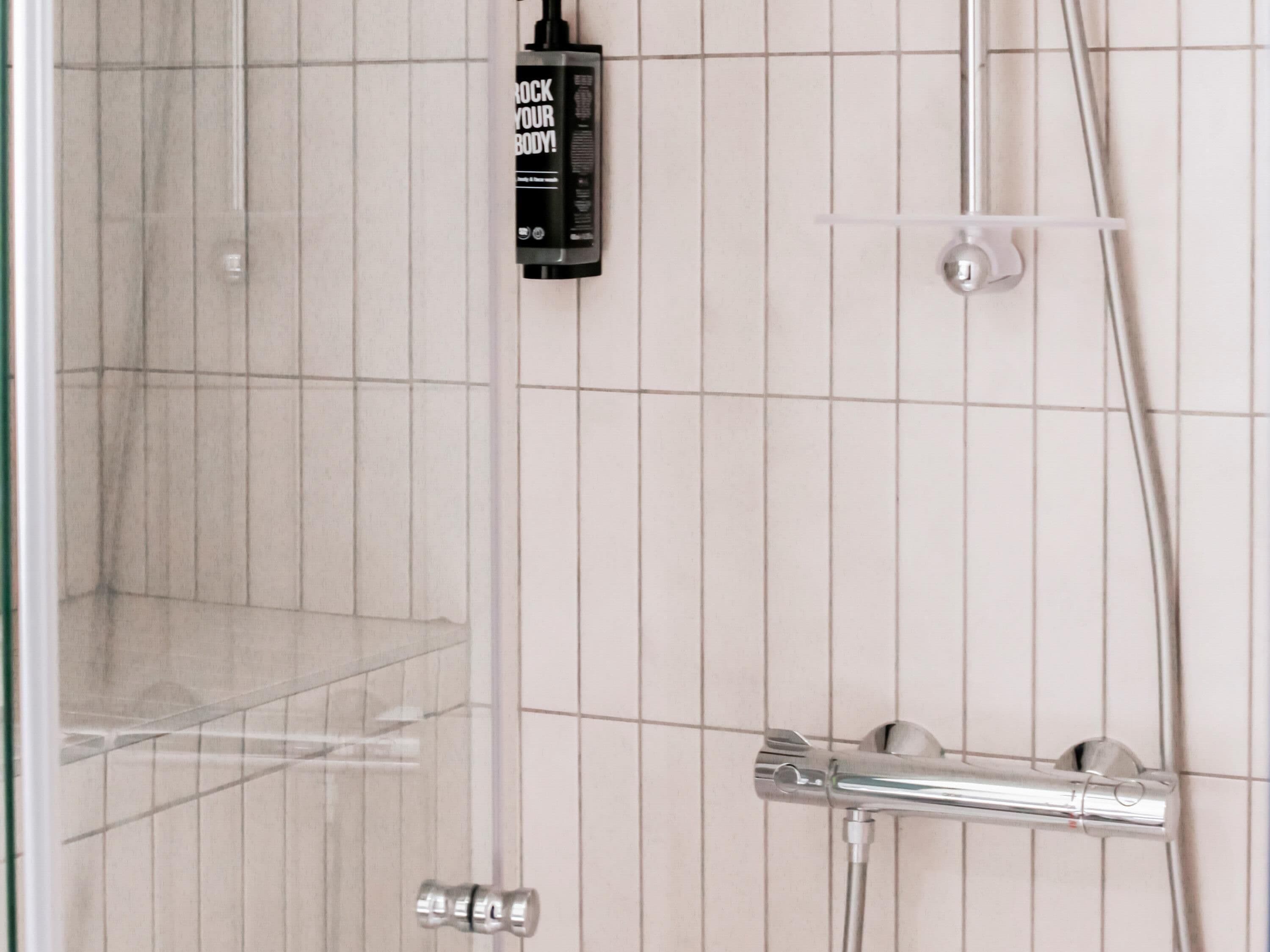 A shower area with a handheld showerhead and a wall-mounted control panel.