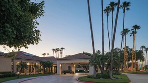 A hotel entrance with a covered patio, palm trees, and a curved driveway.