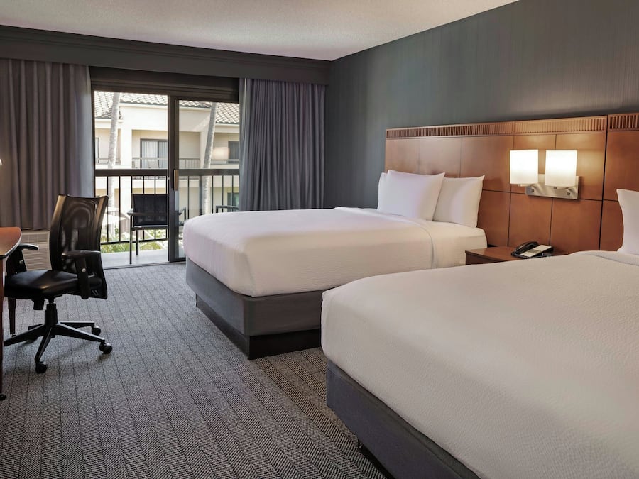 A hotel room with two beds, a desk with a chair, a phone, and a window with curtains.