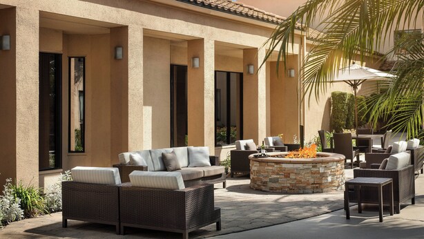 An outdoor patio with wicker furniture, a stone fire pit, and a covered seating area.