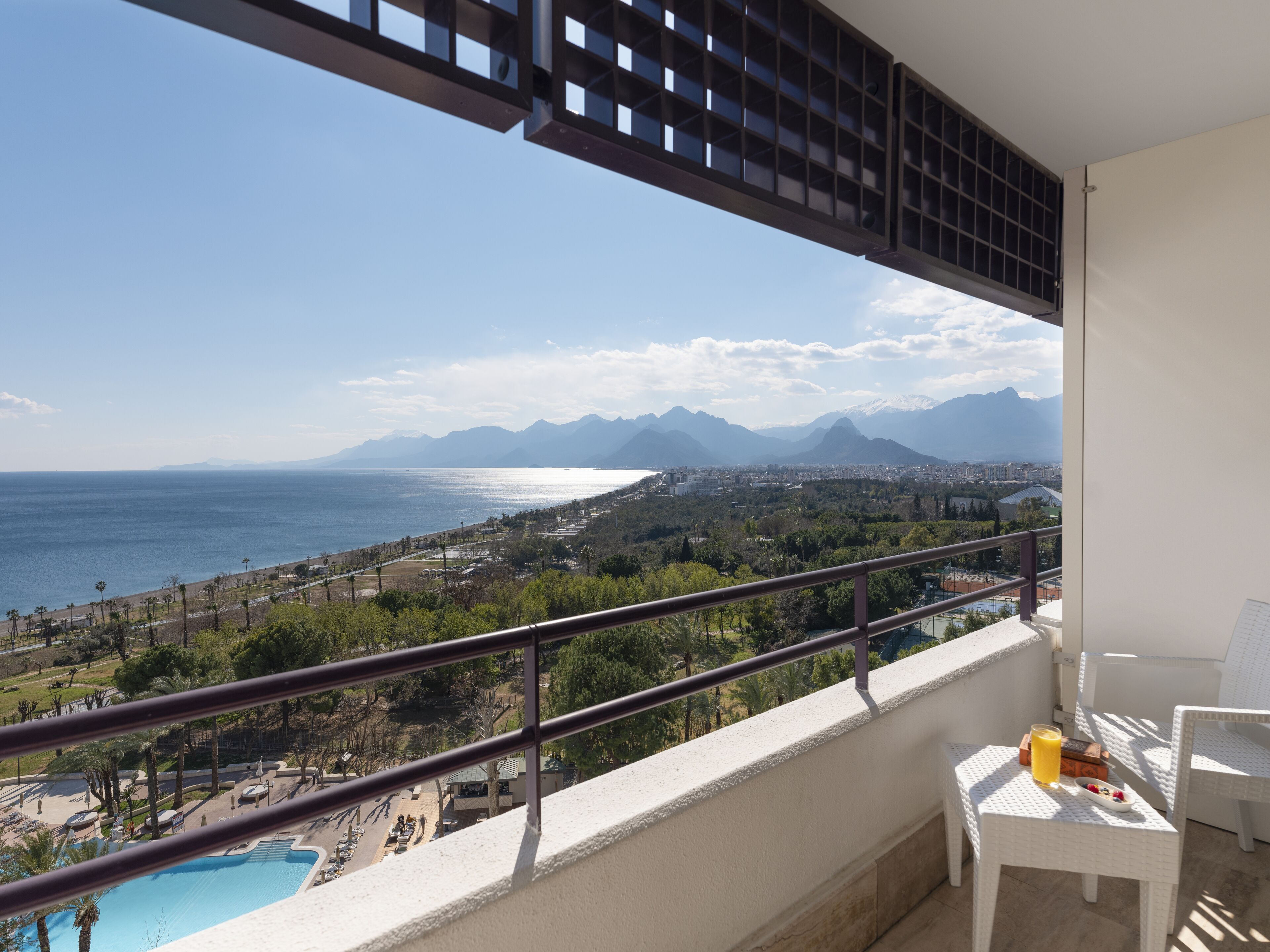 Un balcón con vistas a una playa, una piscina y montañas.