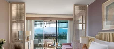 Une chambre d’hôtel avec un grand lit, un bureau, une chaise, une table avec un vase et une vue sur une montagne, visible à travers la porte vitrée.