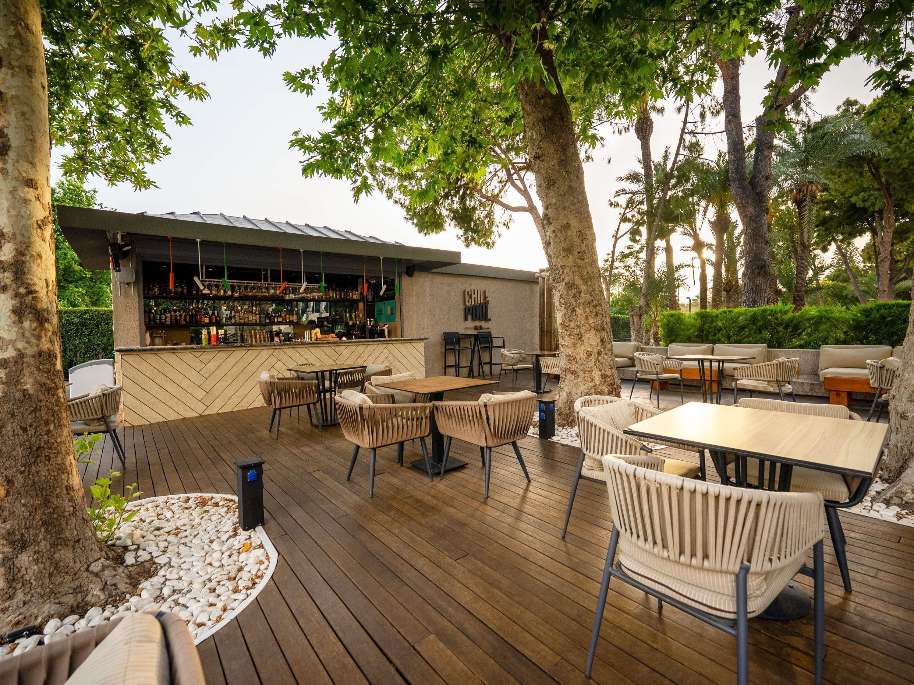 Um pátio externo com piso de madeira, móveis de vime e um espaço de bar.