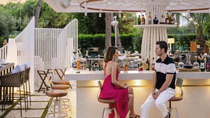 Un espace bar extérieur doté d’une structure blanche portant l’inscription « Turunc », comprenant un comptoir, des tabourets et une variété de bouteilles et de verres.
