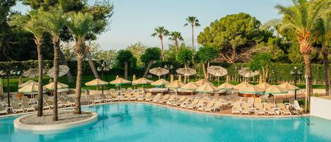 A pool area with lounge chairs and umbrellas, surrounded by trees.